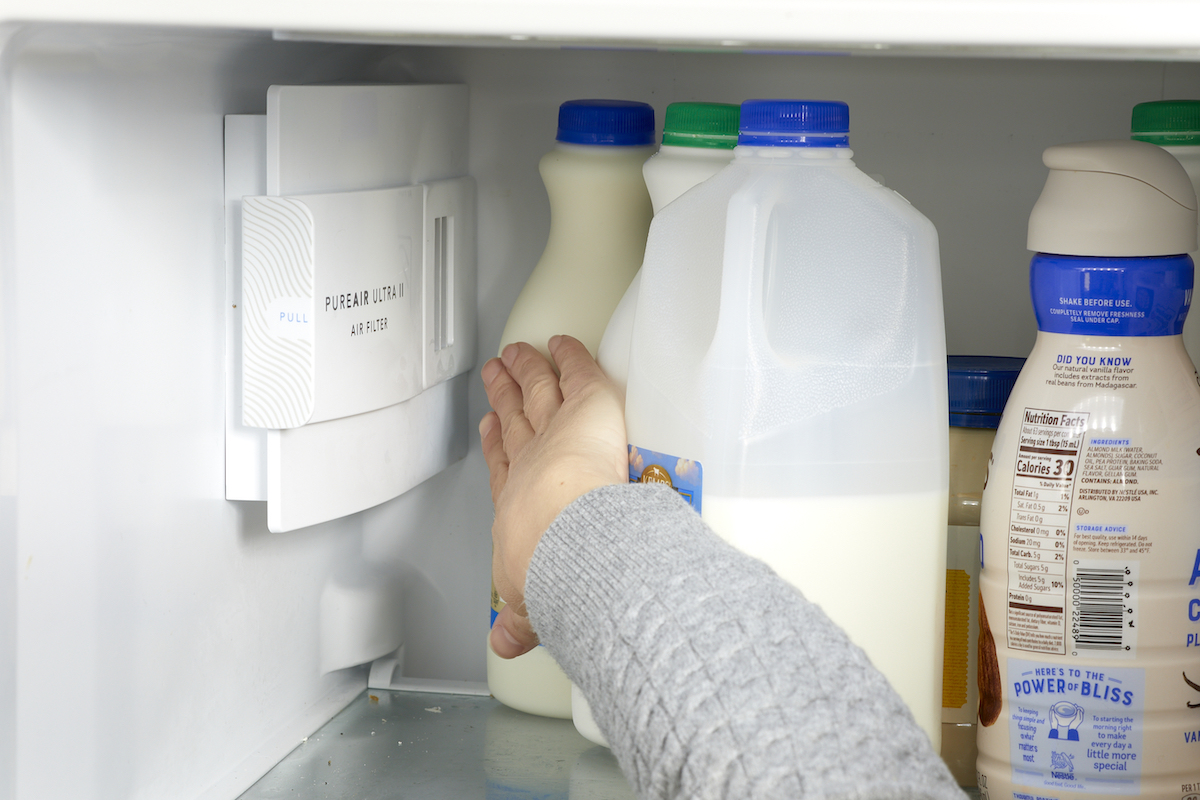 Woman moves milk and other refrigerator items away from the appliance's air vent.