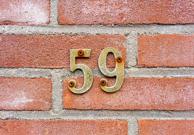 Rusted screws on address numbers in a brick wall.