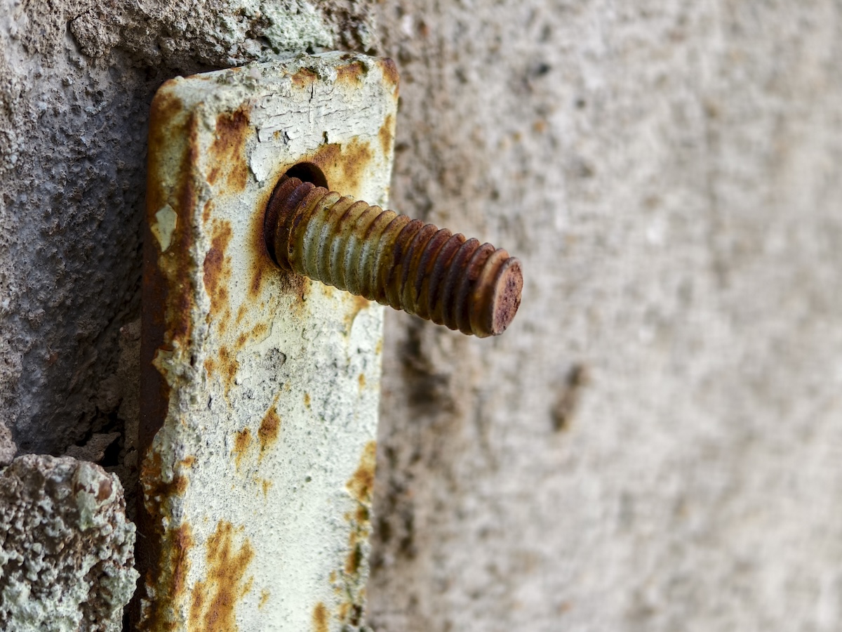 A partially rusted screw in a cement wall.
