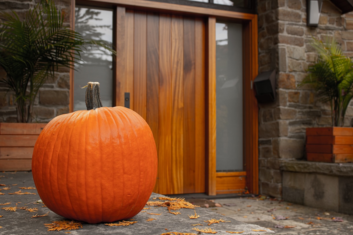 Large pumpkin outside the wood front door of a modern wood-and-glass entryway.