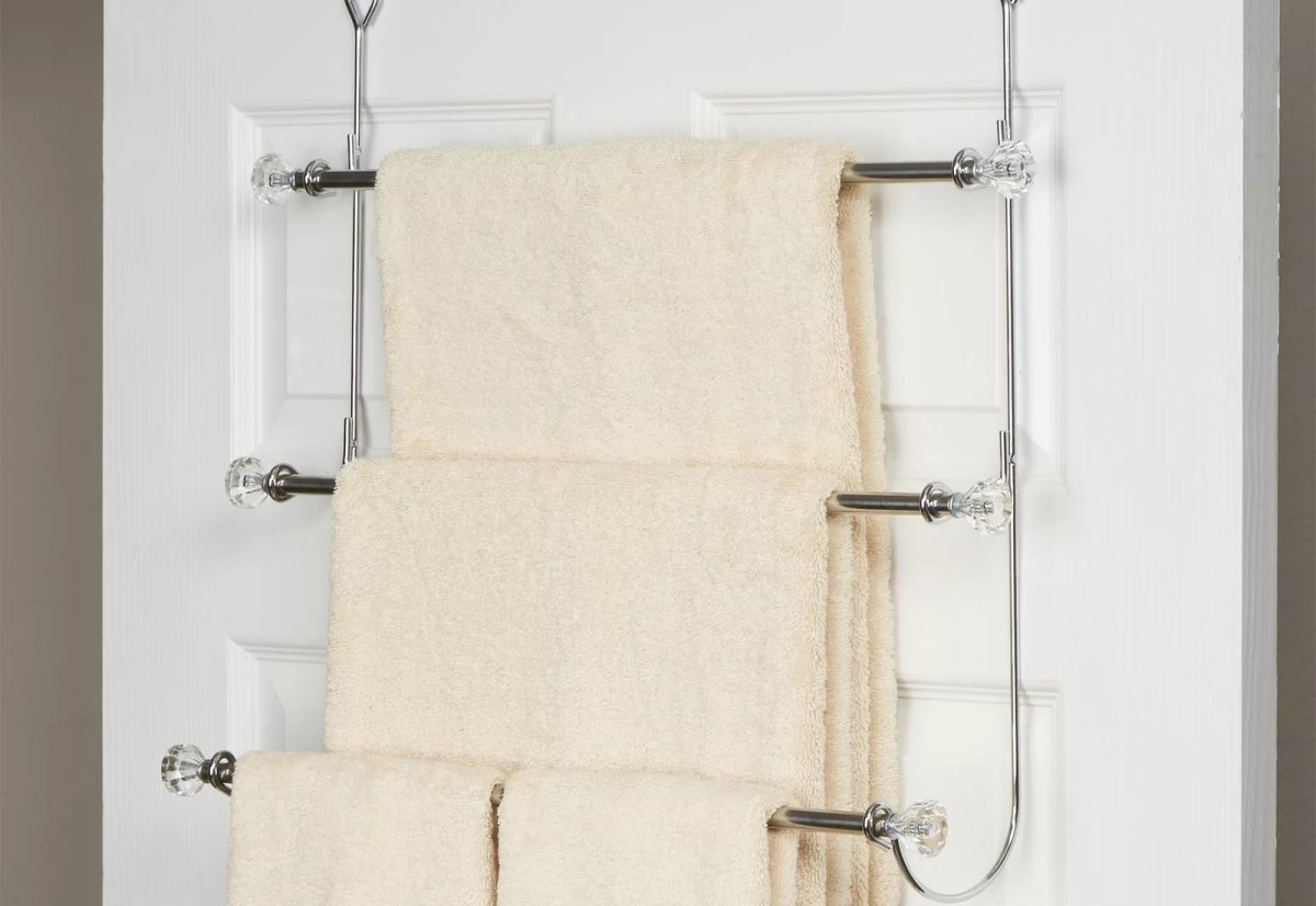 Cream colored towels on a multi-tiered over-the-door towel rack.
