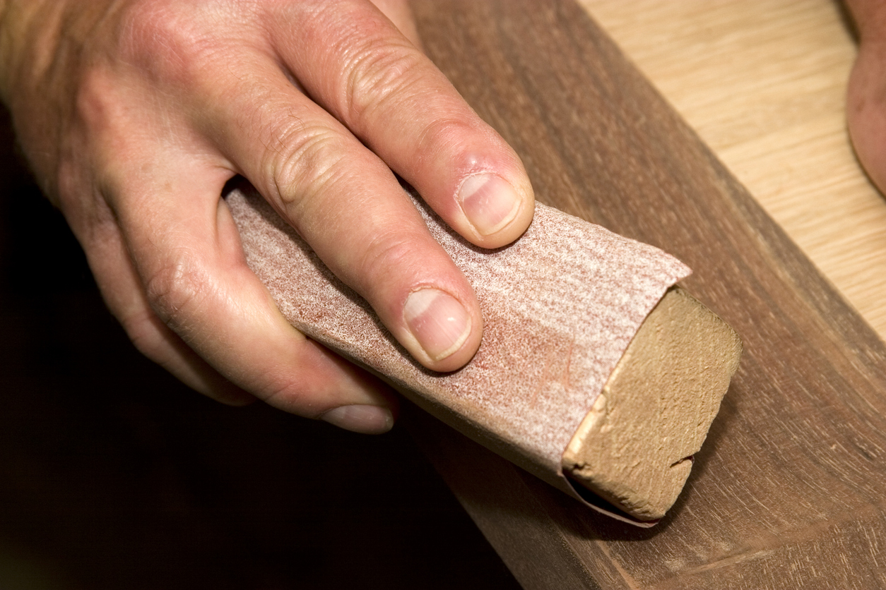 Close-up of a man sanding wood by hand in the workshop.