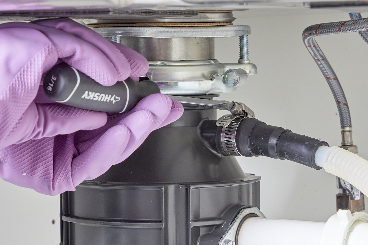 Person wearing rubber gloves tightens a screw on a clamp on a garbage disposal pipe.