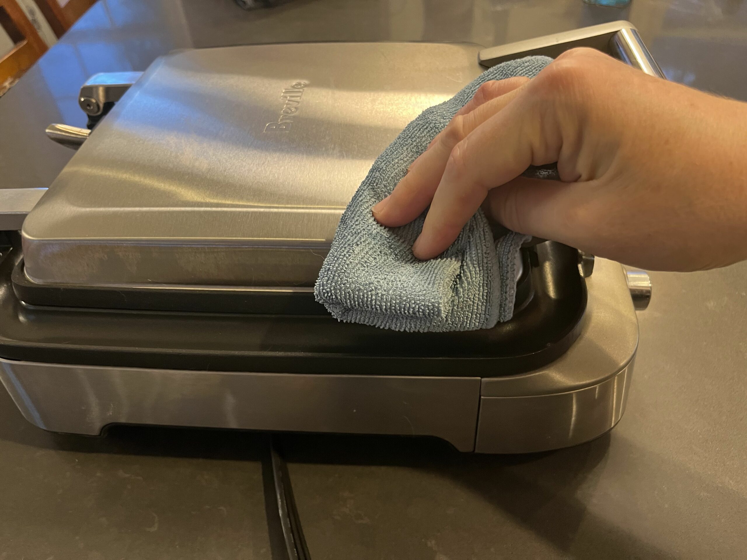 Close up of hand wiping down outside of waffle maker