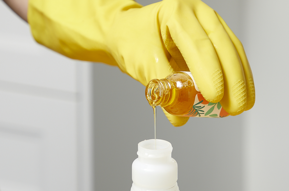 Woman wearing yellow rubber gloves pours essential oil into a spray bottle.