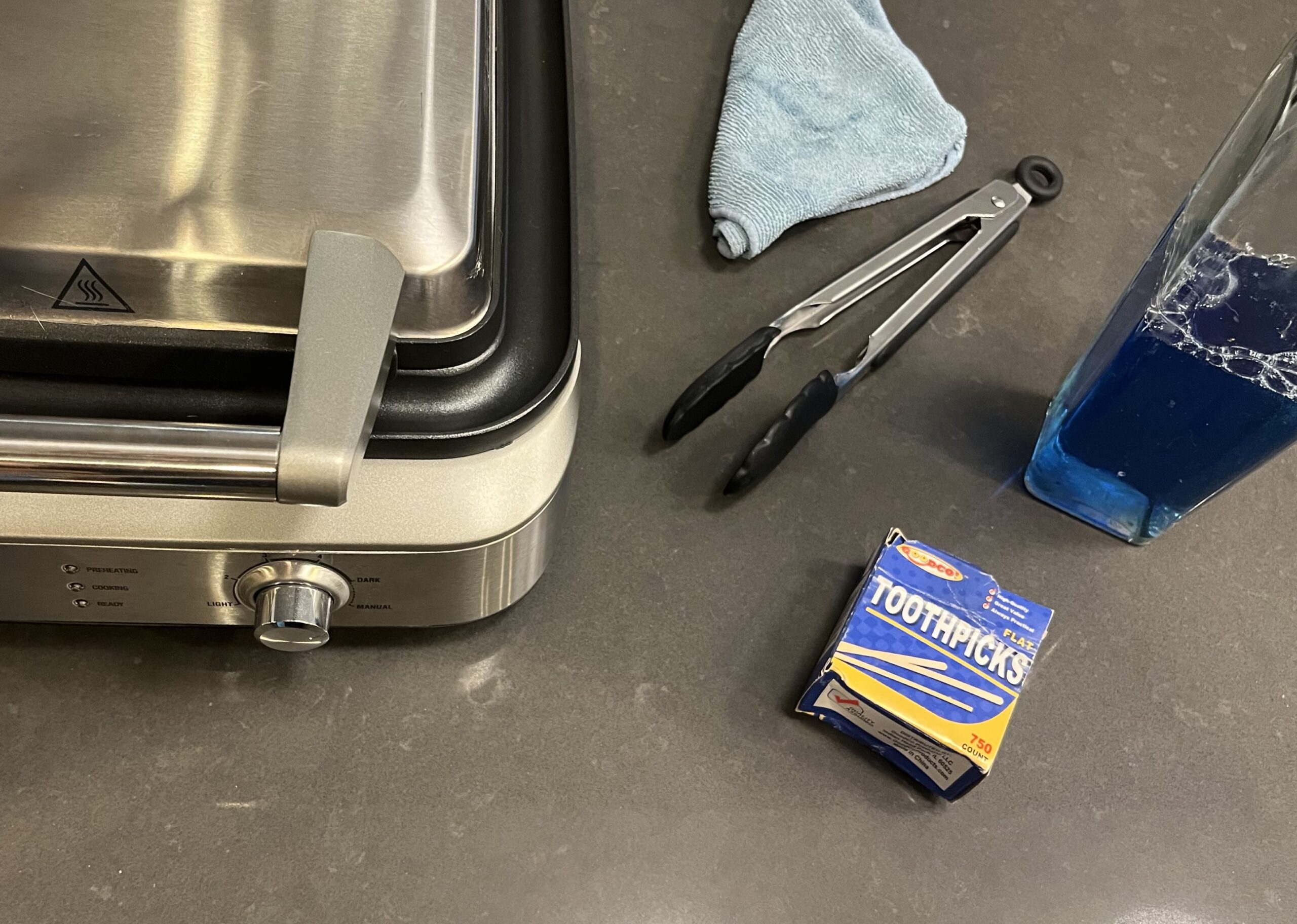 Stainless Breville waffle maker and cleaning supplies on kitchen counter.