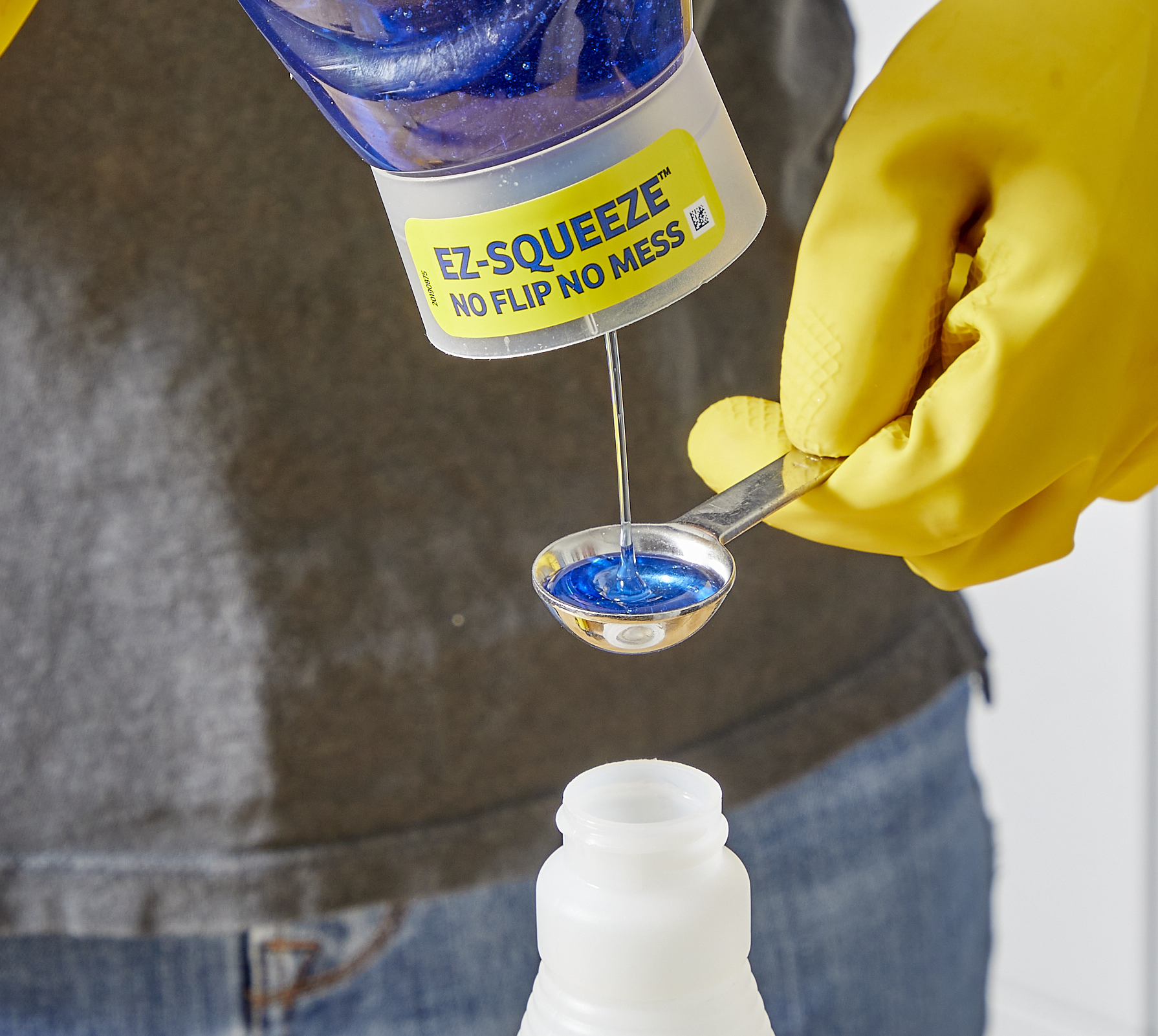 Woman wearing yellow rubber gloves pours dish soap into a measuring spoon above a spray bottle.