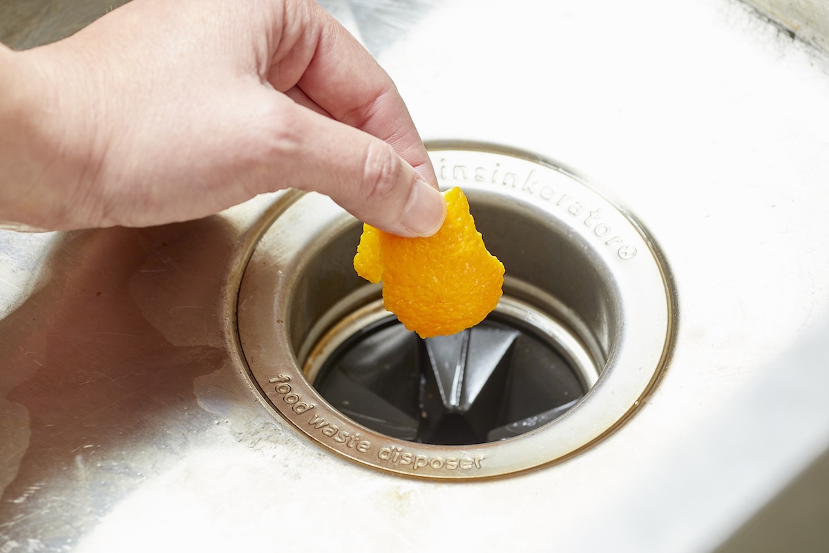 Person drops orange peel into a sink's garbage disposal.