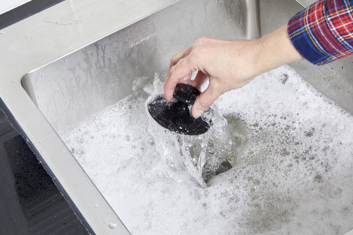 Person pulls drain plug out of stainless steel sink full of soapy water.