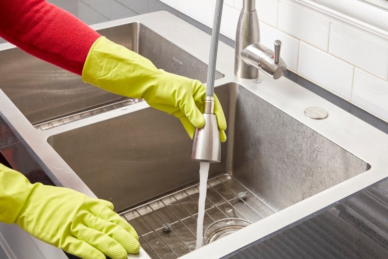 Woman wearing cleaning gloves sprays water into sink from faucet.