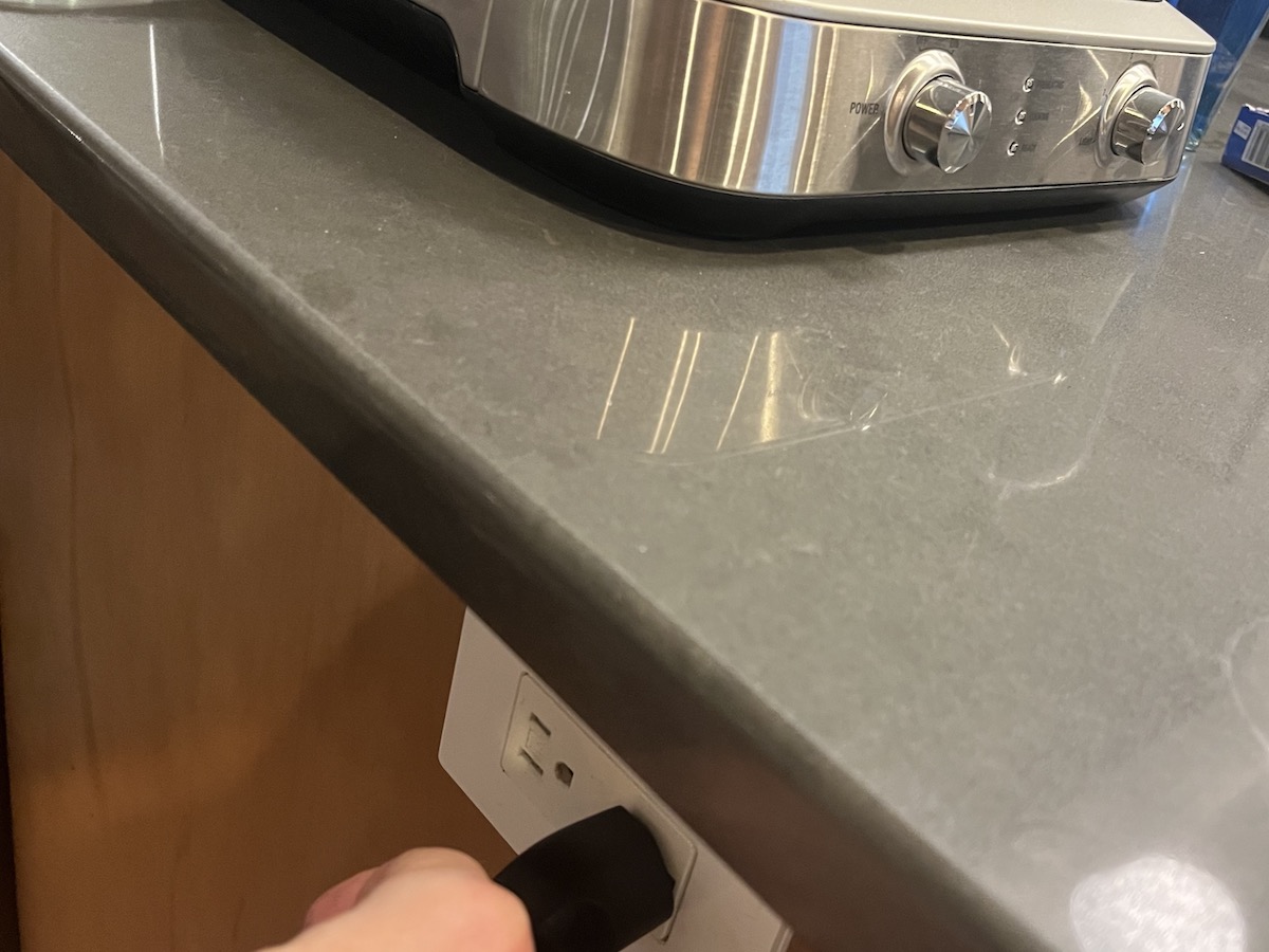 Person unplugging a stainless steel waffle maker from electrical outlet.