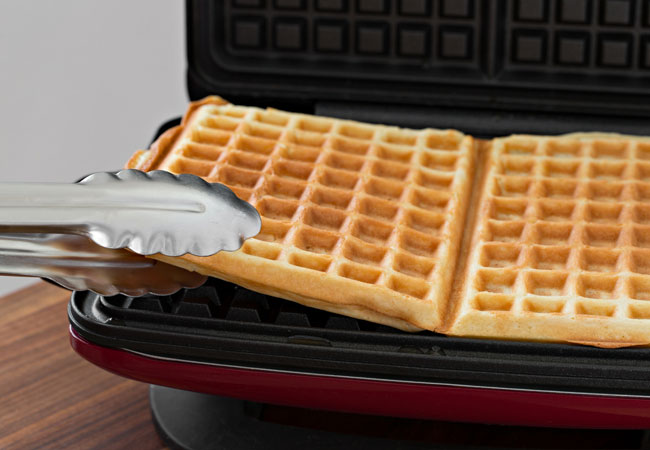 Using tongs to remove a waffle from a waffle iron
