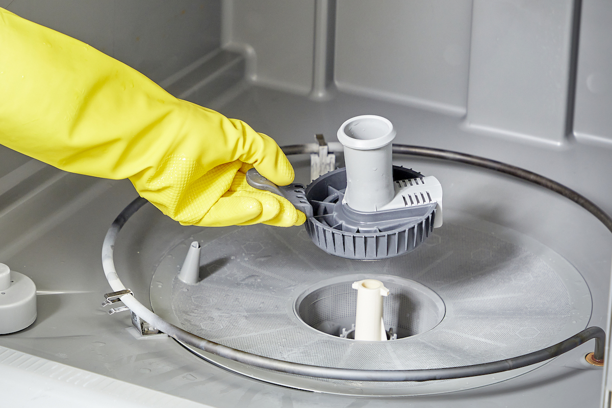 Woman wearing rubber gloves returns clean dishwasher filter to dishwasher.