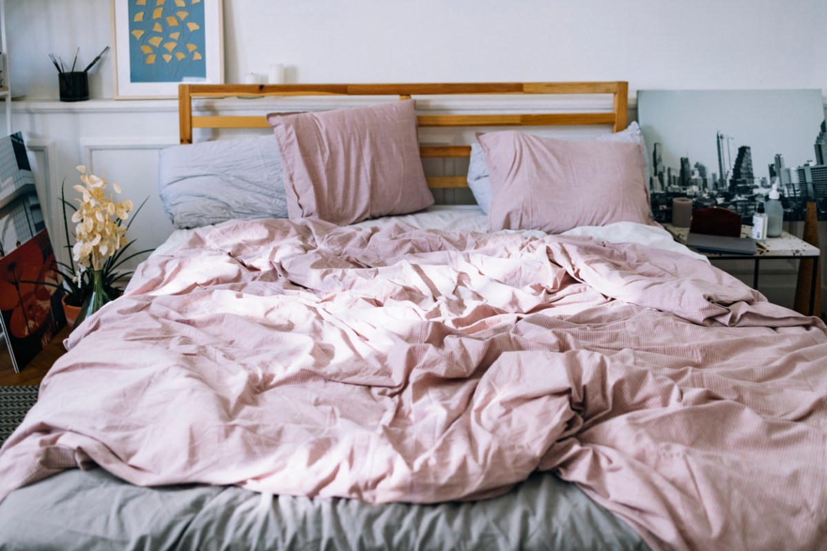 view from end of bed with wood frame baseboard with pink sheets and pillowcases