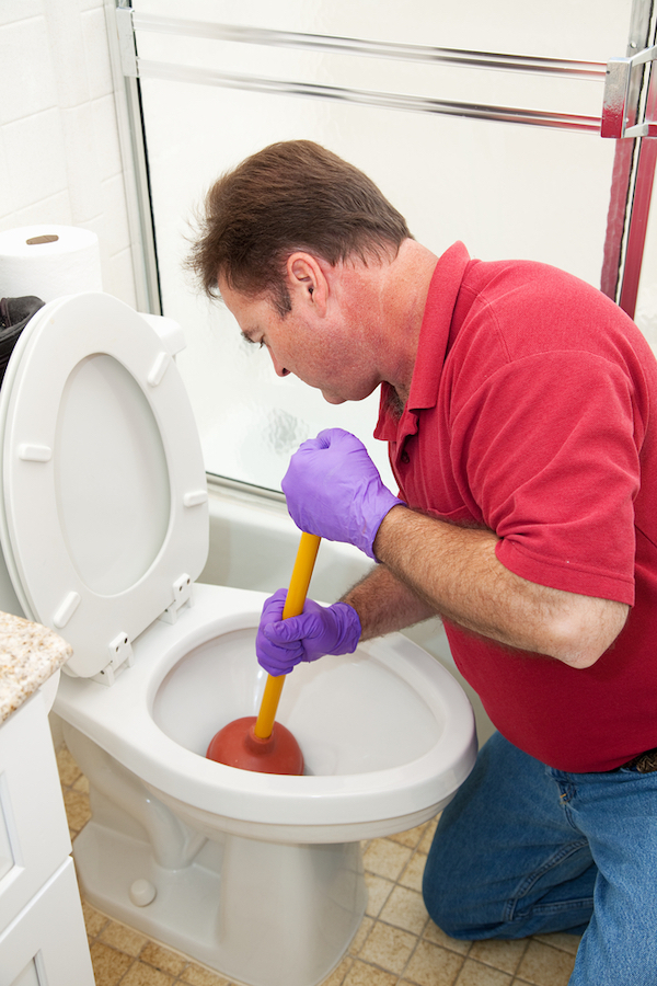 man wearing rubber gloves plunging a toilet