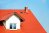 Close-up of red roof tiles, brick chimney and dormer window.
