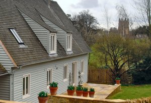 A timber clad house with a gravel drive and lucarne dormers.