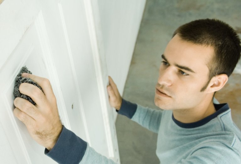 Man uses steel wool to sand a white interior door.