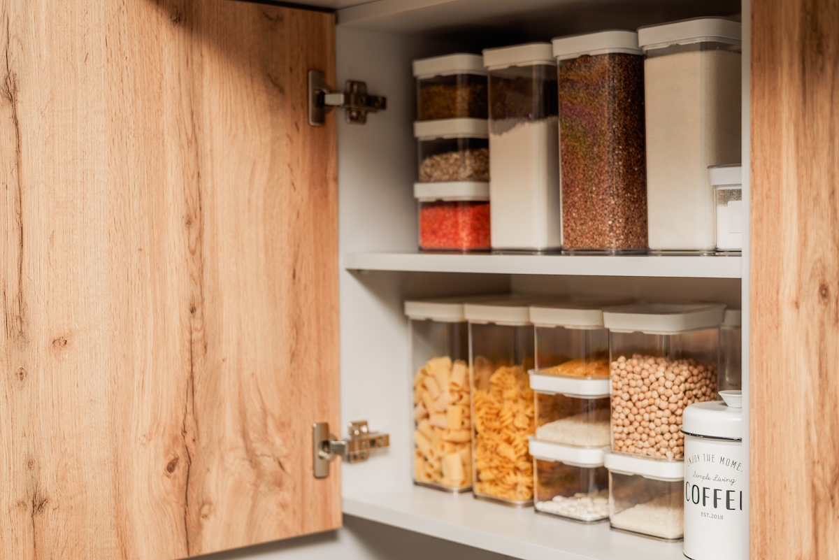 Dry pantry goods in sealed plastic food containers organized neatly inside a wood kitchen cabinet.