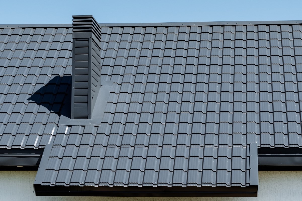 Composite material roof with chimney against blue urban sky.
