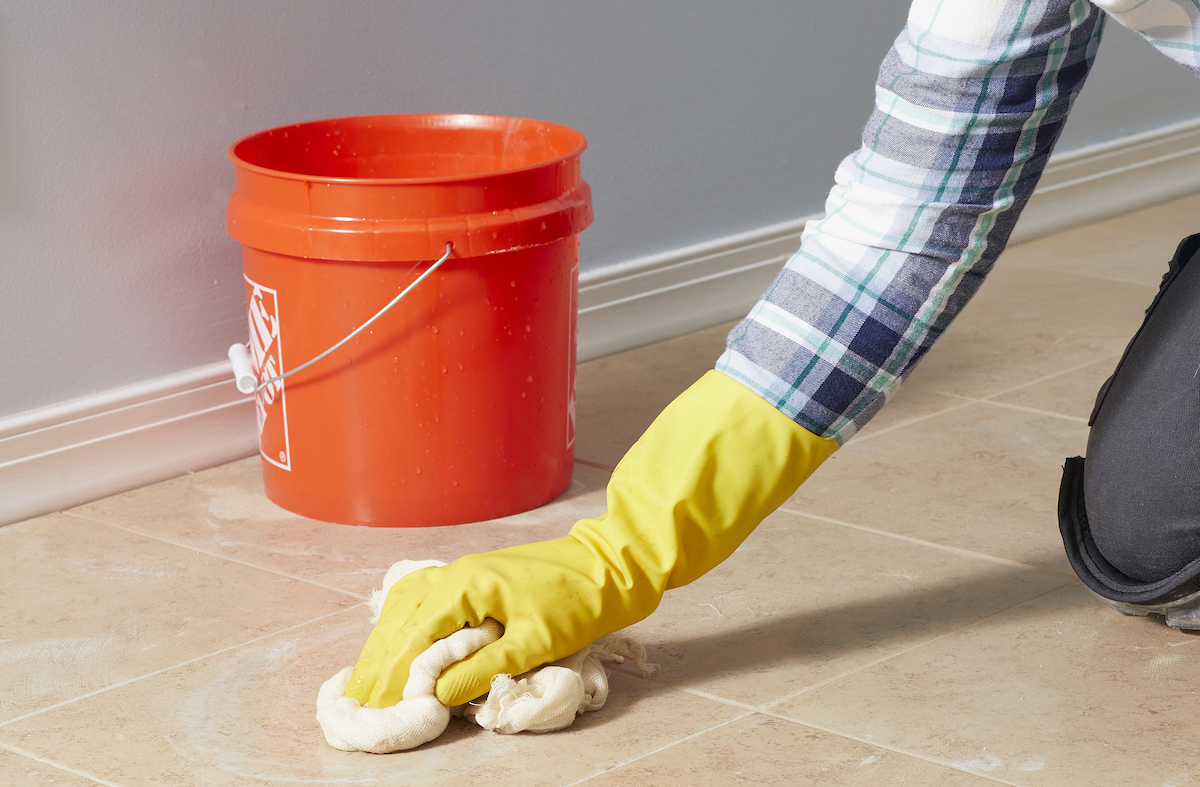 Woman wearing rubber gloves wipes floor with a cheesecloth, an orange bucket in the background.