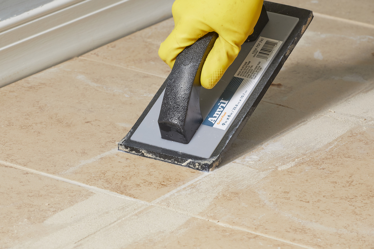 Person wearing yellow goves uses a grout float at an angle on a tile floor.