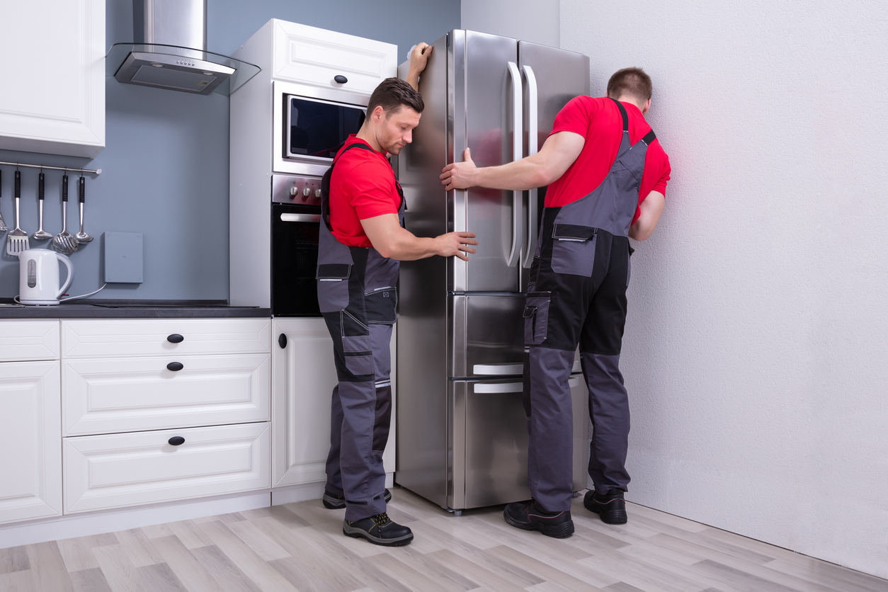 two men moving a new refrigerator in kitchen