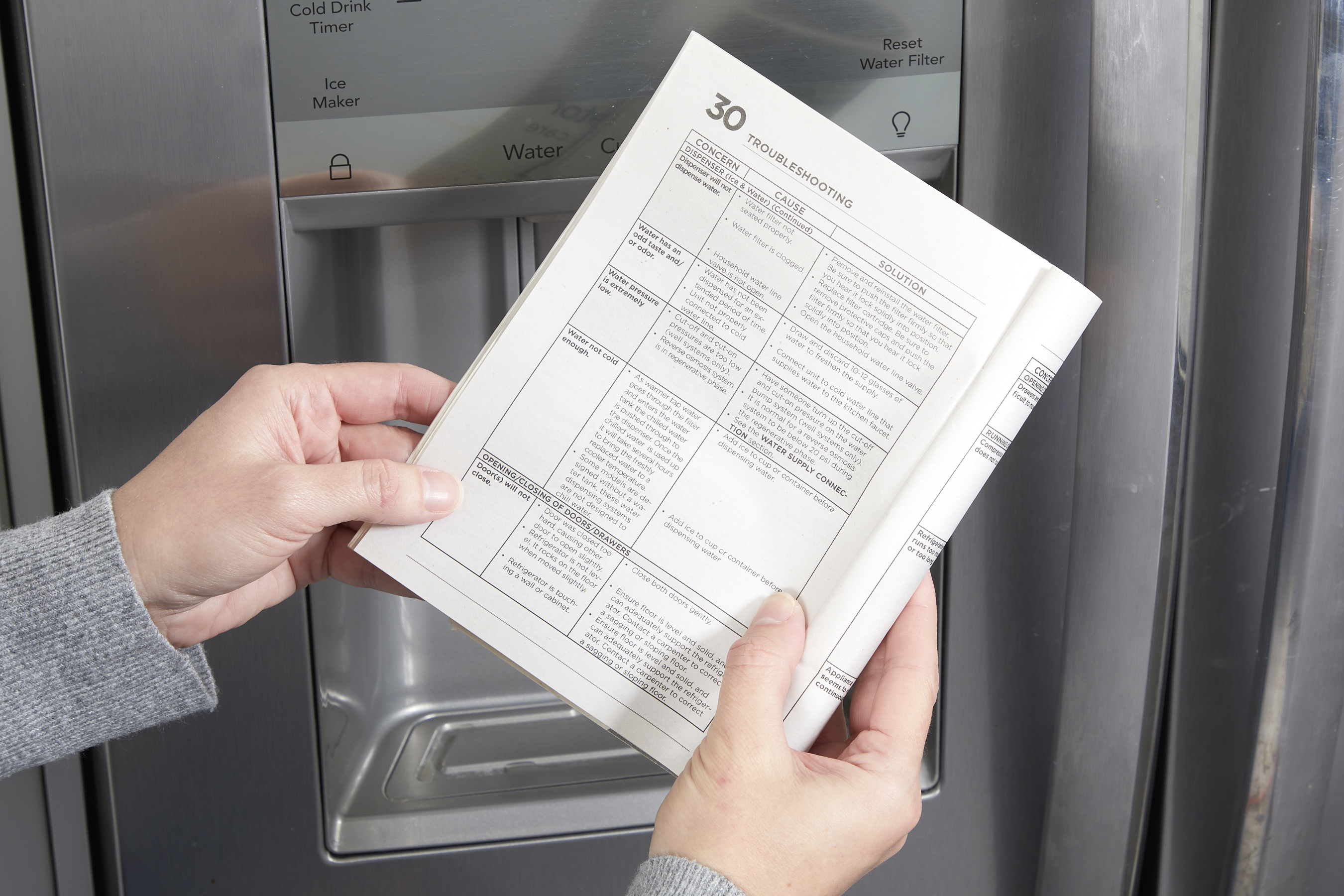 Woman holding a refrigerator manual in front of the appliance.
