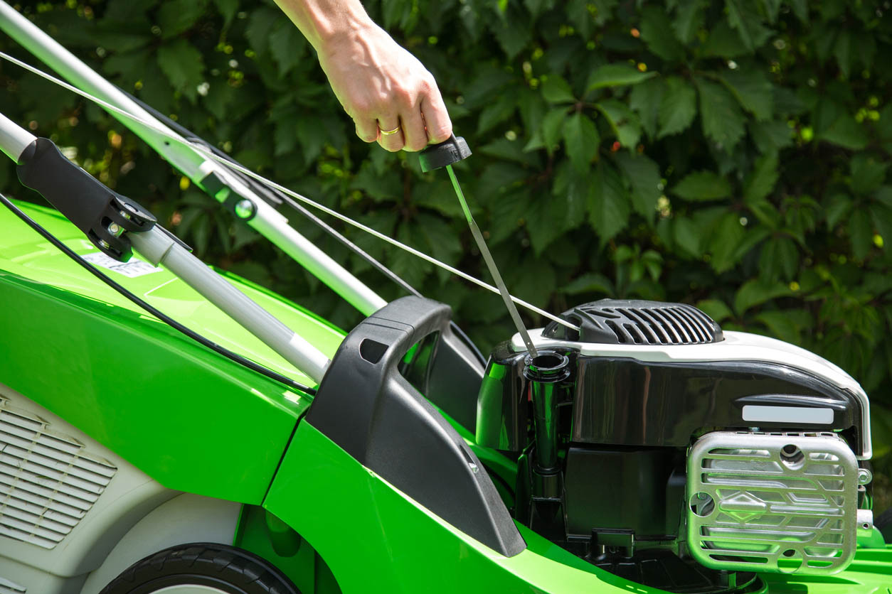 Using a dipstick to check the oil in a bright green lawnmower. 