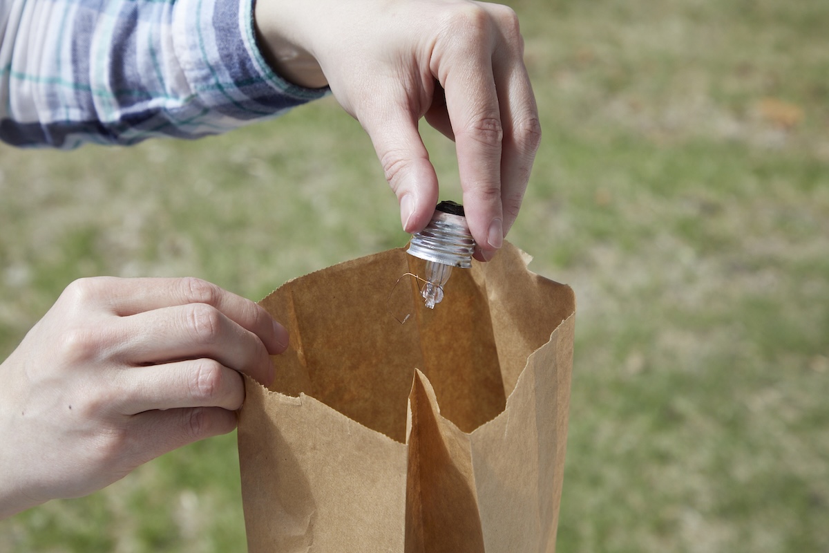 Woman puts the remains of a broken light bulb into a brown paper bag.