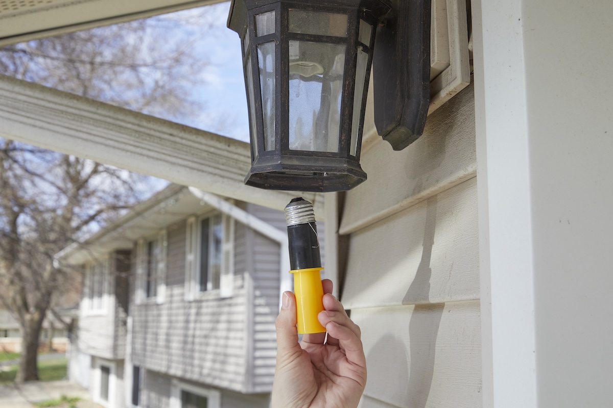 Woman maneuvers a light bulb extractor into an outdoor light sconce.