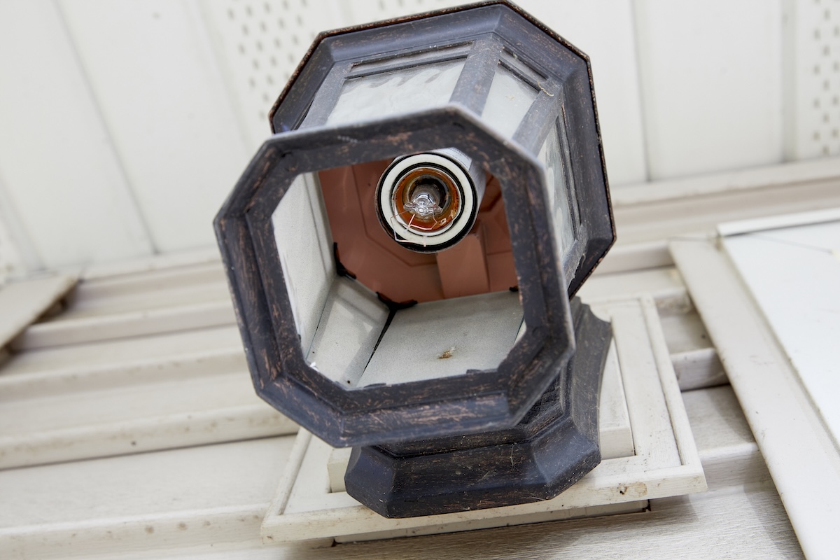 Ground-level view looking up into an outdoor sconce in which a light bulb broke in the socket.