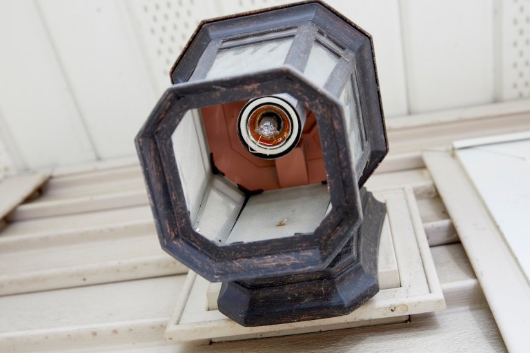 Ground-level view looking up into an outdoor sconce in which a light bulb broke in the socket.
