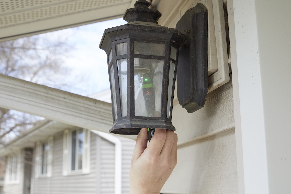 Woman reaches into an outdoor sconce with a multimeter to confirm that the power to a socket is off.