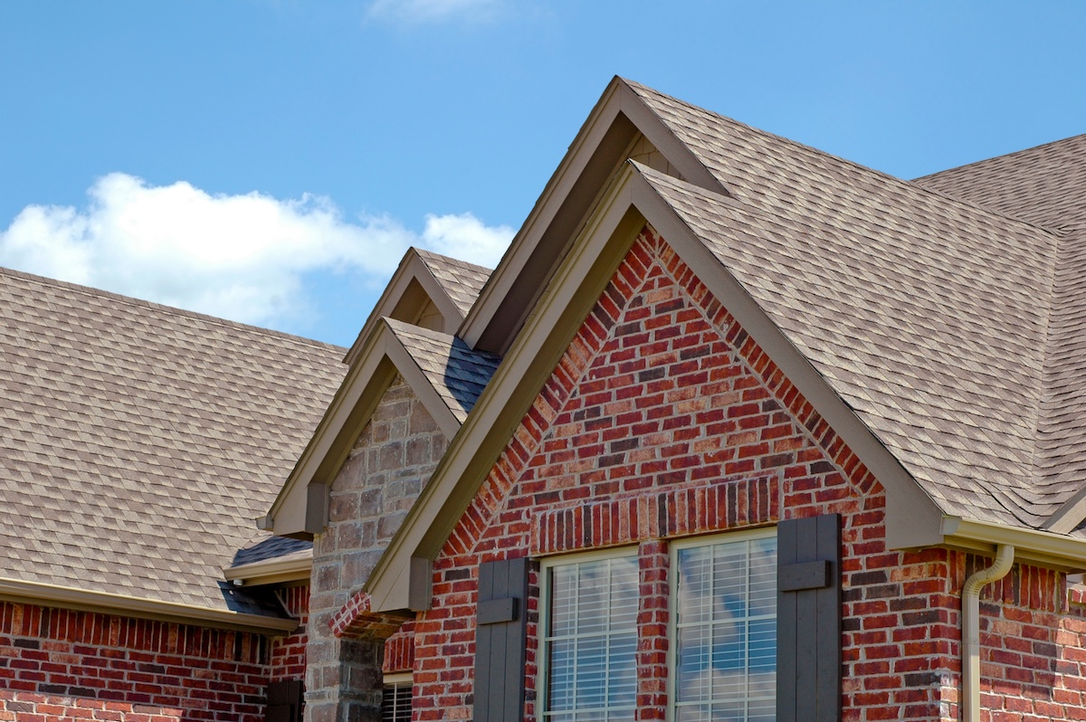 Roof line of a red brick house with gables. Roof has brown asphalt shingles.