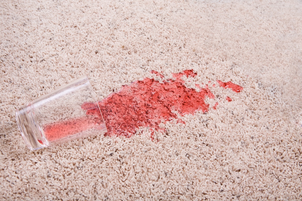 A bright red liquid spills out of a glass and onto beige carpet.
