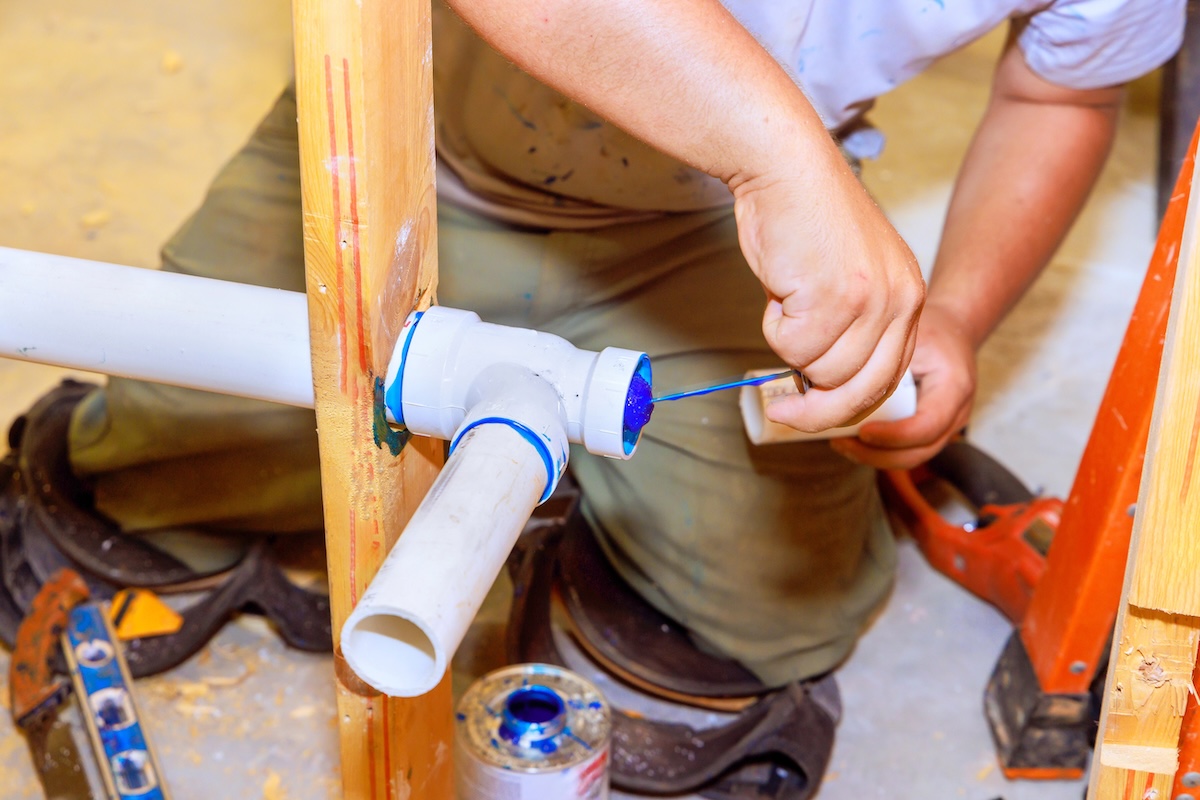 Plumber applies glue inside PVC drainage pipes that are inside new construction wall studs.