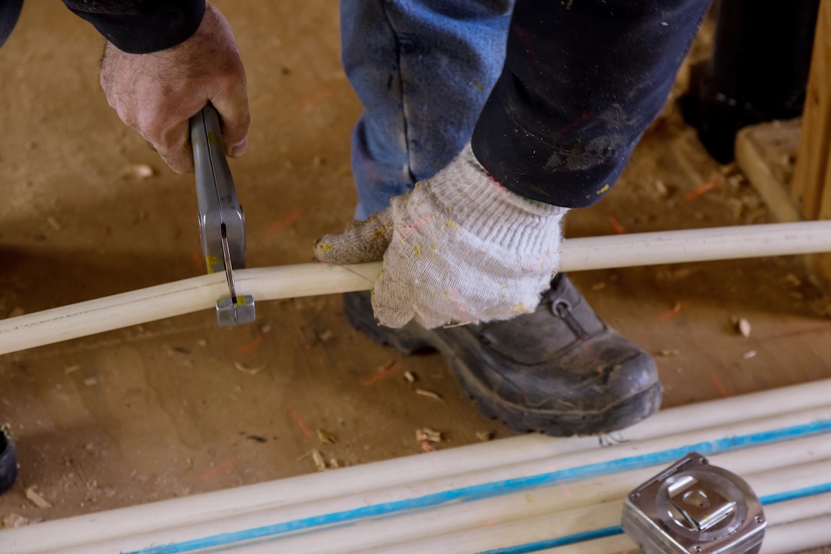 Plumber cutting in the PVC water lines pipe with a pipe cutter.