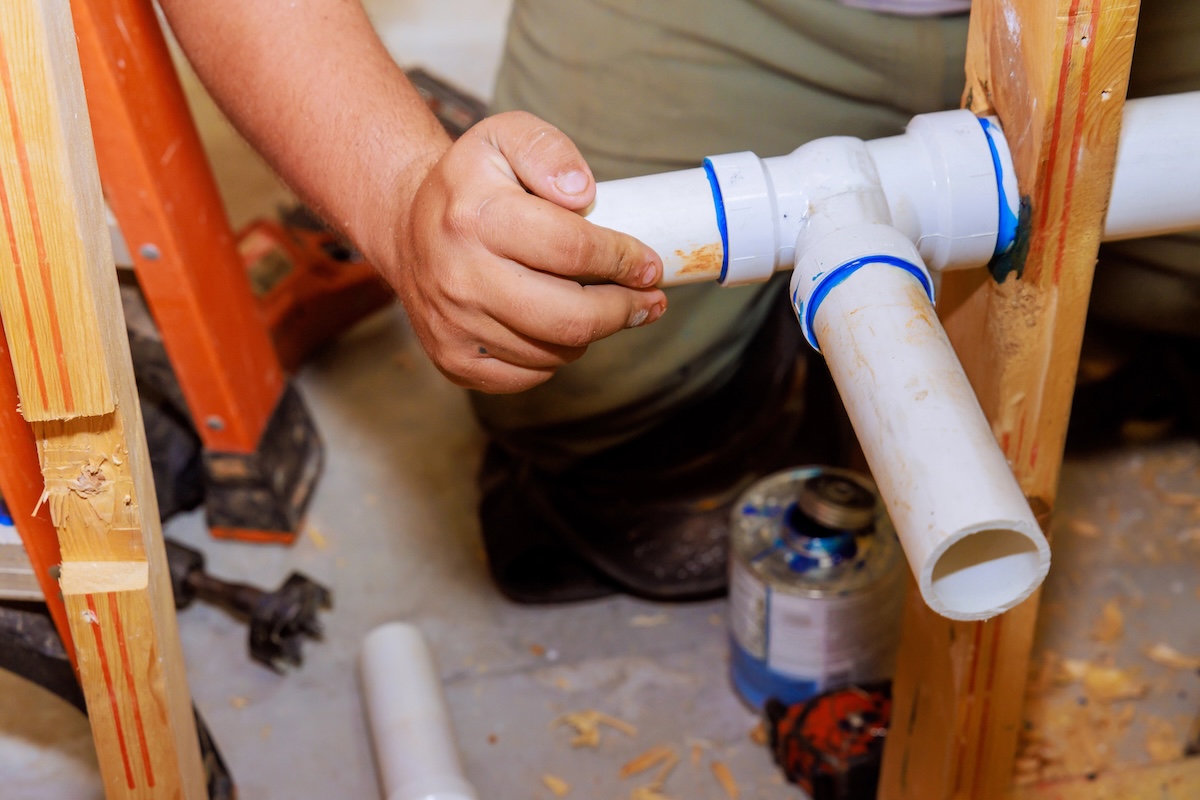 Plumber holds end of PVC pipe into joint with other pipes to allow glue to set.