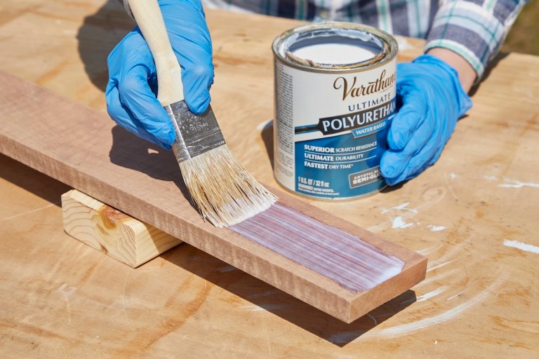 Person wearing nitrile gloves brushes polyurethane onto a board outdoors.