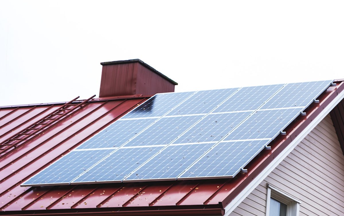 A solar panel is on a red metal roof of a house.