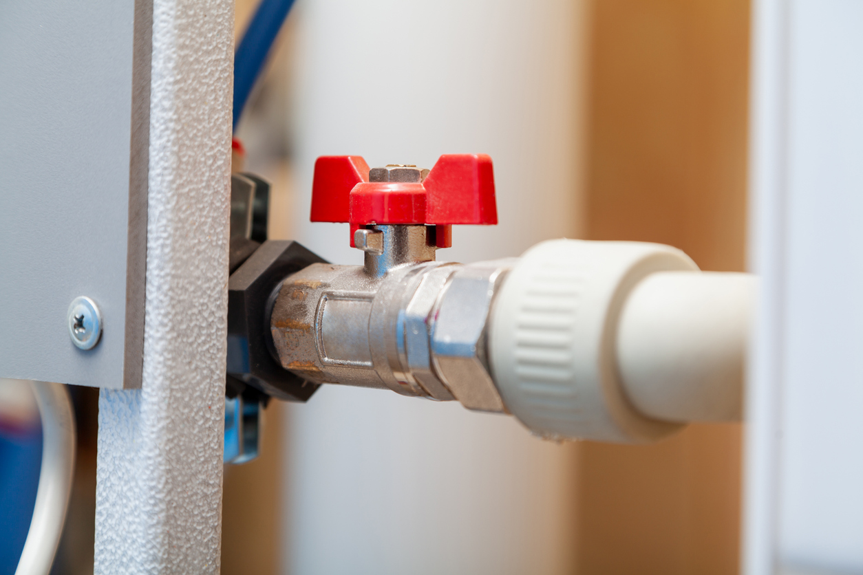 A close-up of a horizontal plastic pipe with red gate valve.