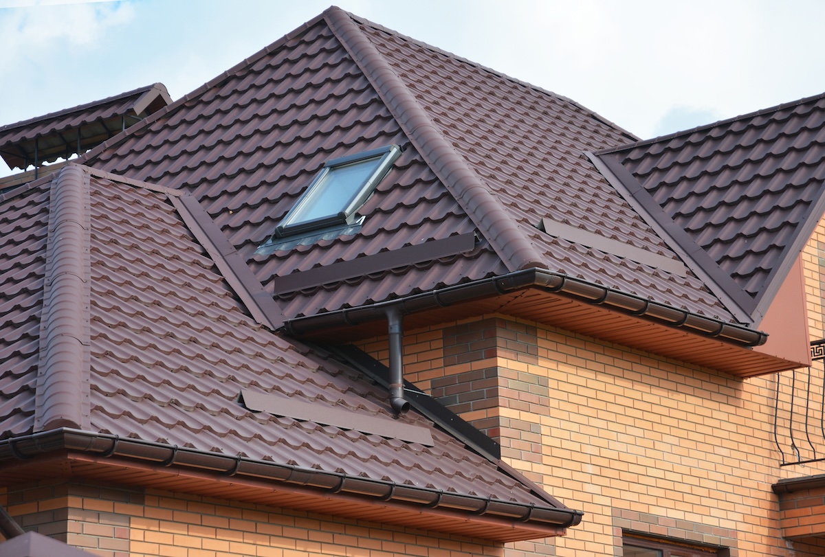 A metal tiled roofing with complex angled construction with a skylight on a brick house.