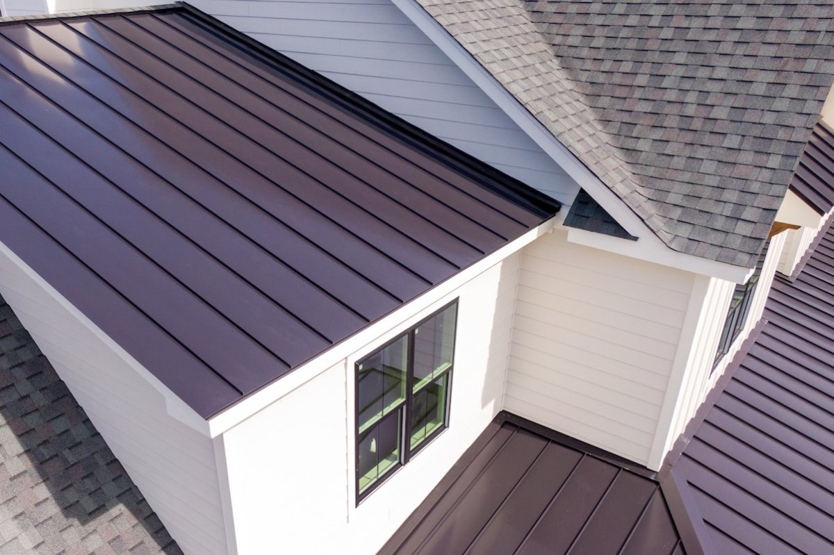 Overhead view of multiple angles of the roof a white house, some covered with metal roofing and some with asphalt shingles.