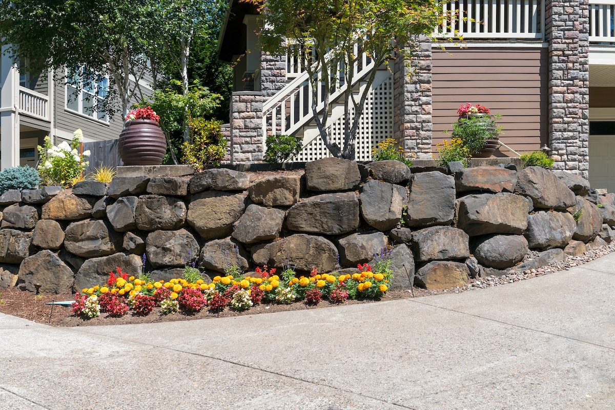 A house with flower garden beds in front, all surrounded by a stone retaining wall.  