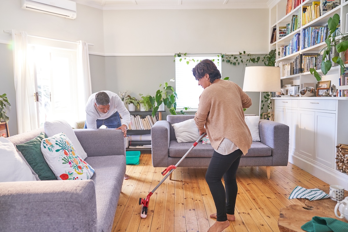 A mature couple uses a reusable mop to clean their hardwood floors in a living room.