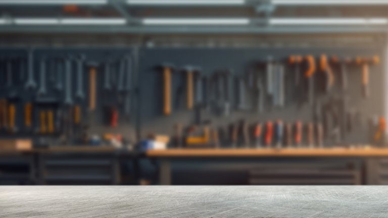 A scratched steel surface in the foreground with a garage interior with workbenches and tools in the background.