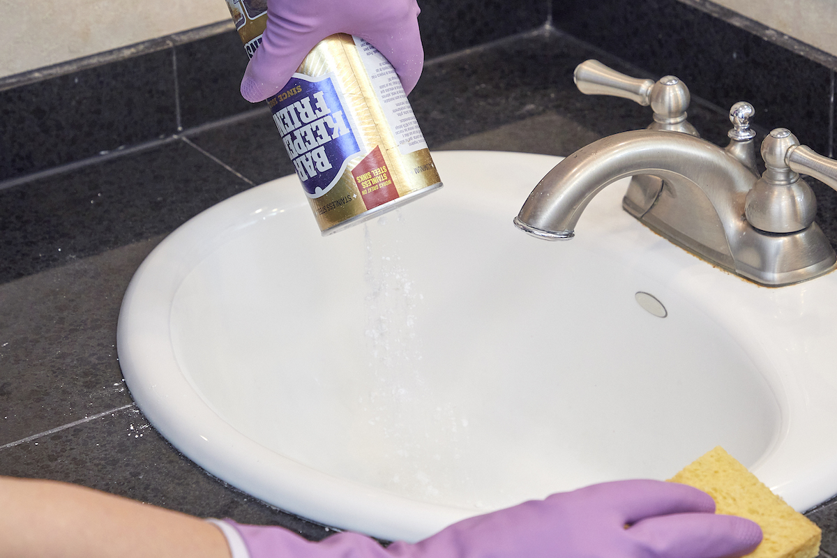 Woman uses Bar Keepers Friend to clean a porcelain bath sink. 