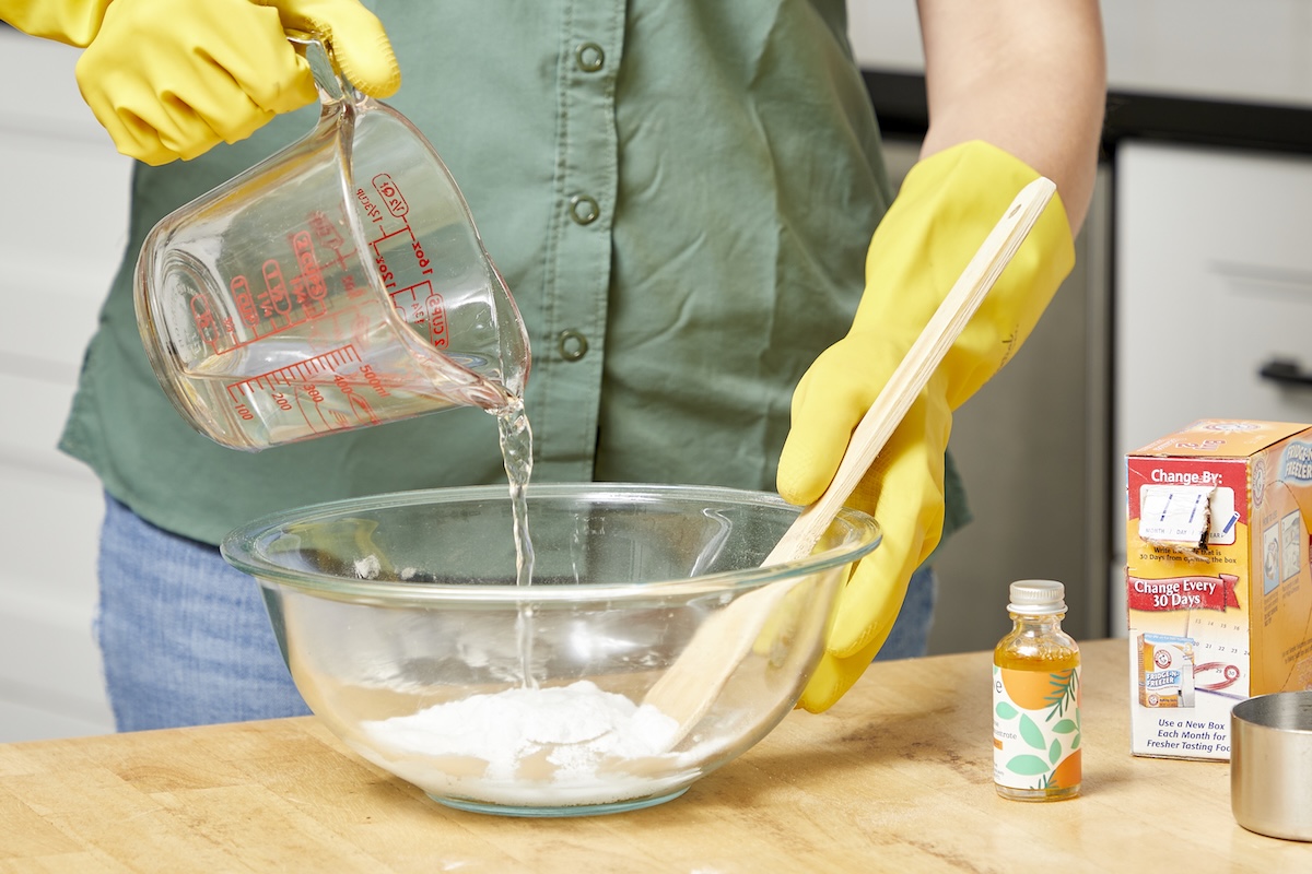Woman mixes baking soda, essential oil, and water in a glass bowl.