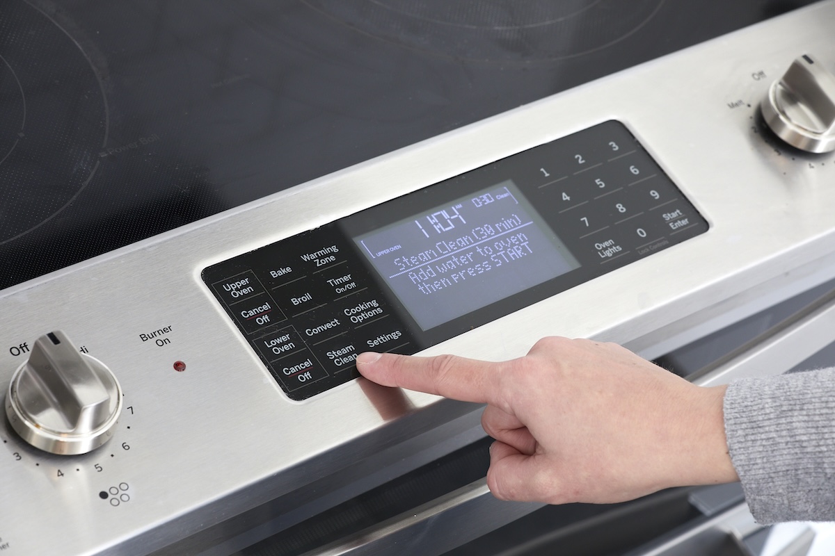 Person pushes the "steam clean" button on an oven's control panel.